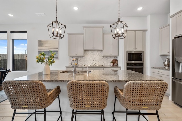 kitchen with appliances with stainless steel finishes, dark stone counters, a sink, and backsplash