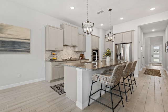 kitchen featuring stainless steel appliances, a breakfast bar, a sink, visible vents, and tasteful backsplash