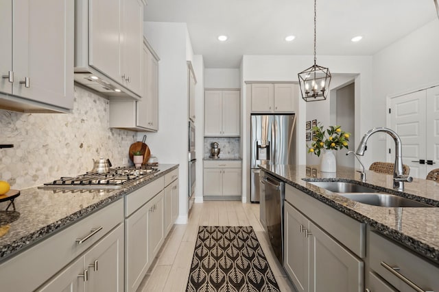 kitchen with decorative light fixtures, gray cabinetry, appliances with stainless steel finishes, a sink, and dark stone countertops