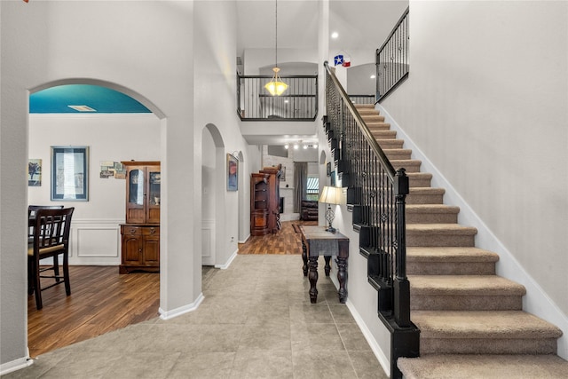 foyer entrance featuring arched walkways, a decorative wall, a high ceiling, wood finished floors, and stairs