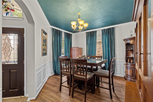 dining room featuring arched walkways, wood finished floors, an inviting chandelier, crown molding, and a decorative wall