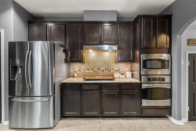 kitchen with arched walkways, under cabinet range hood, dark brown cabinets, appliances with stainless steel finishes, and tasteful backsplash