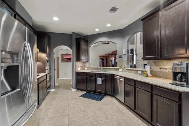 kitchen featuring decorative backsplash, appliances with stainless steel finishes, light tile patterned flooring, dark brown cabinetry, and a sink