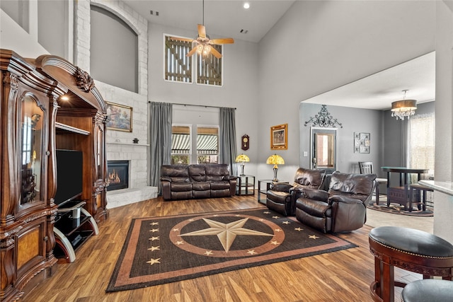 living room with ceiling fan with notable chandelier, a high ceiling, a fireplace, and wood finished floors