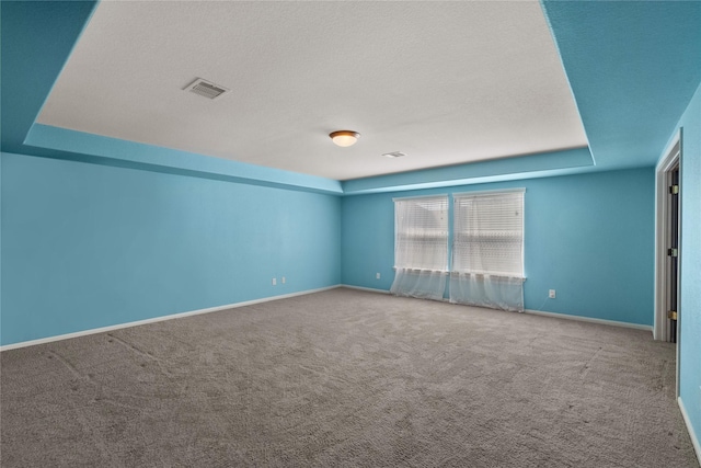 carpeted spare room with a textured ceiling, a raised ceiling, visible vents, and baseboards