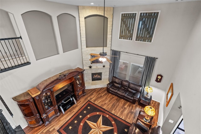 living area featuring ceiling fan, a stone fireplace, and wood finished floors