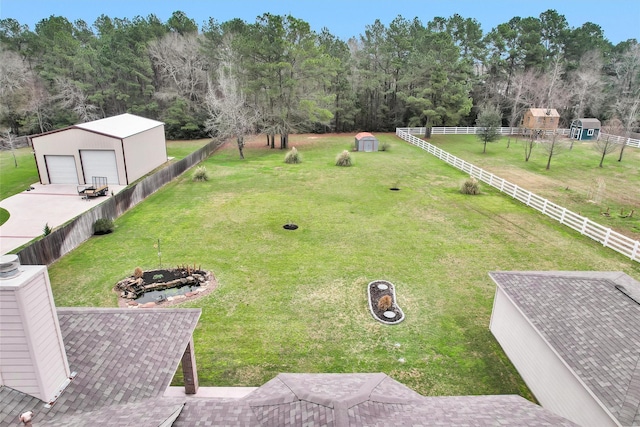 view of yard featuring a fire pit, an outbuilding, a detached garage, and fence