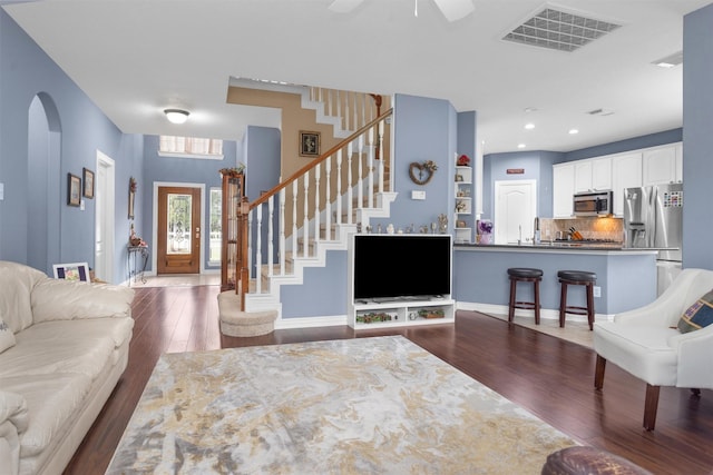 living room featuring dark wood-type flooring, stairway, arched walkways, and visible vents