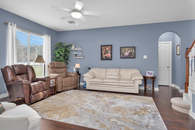 living room featuring a ceiling fan, visible vents, baseboards, arched walkways, and dark wood-type flooring