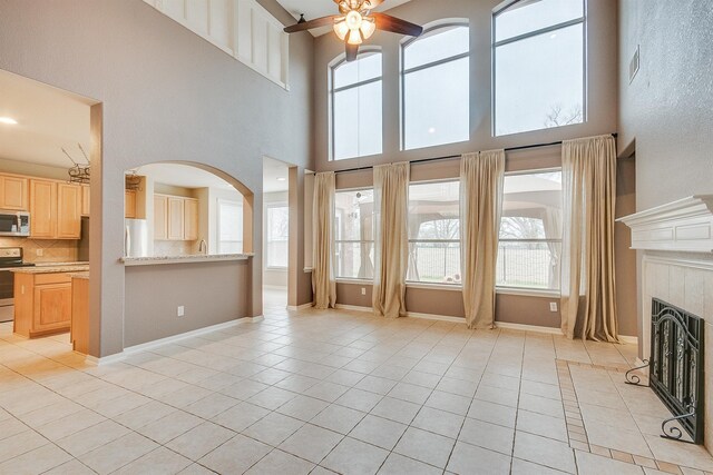 unfurnished living room featuring light tile patterned floors, arched walkways, a tile fireplace, and a healthy amount of sunlight