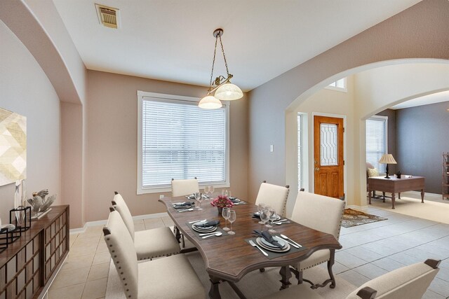 dining space with light tile patterned floors, arched walkways, visible vents, and baseboards