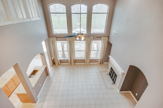 entrance foyer with a high ceiling, a glass covered fireplace, light tile patterned flooring, ceiling fan, and baseboards