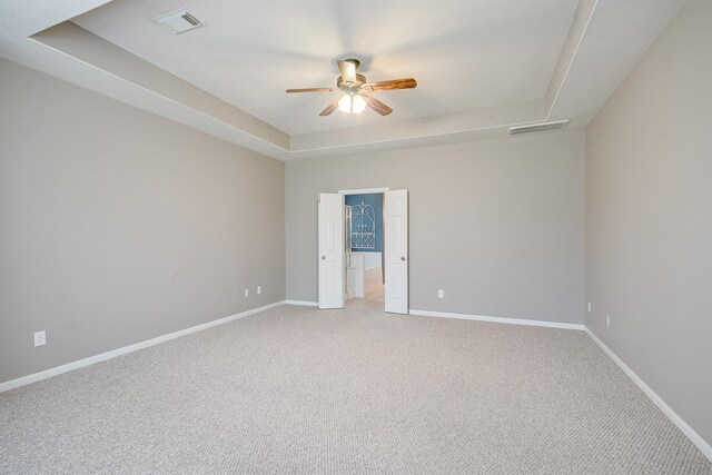 empty room featuring light carpet, a tray ceiling, visible vents, and baseboards