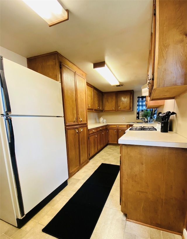 kitchen with brown cabinetry, freestanding refrigerator, light countertops, light floors, and a sink