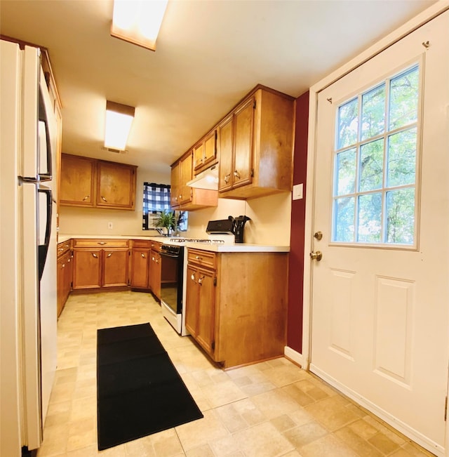 kitchen featuring brown cabinets, light countertops, freestanding refrigerator, gas range, and under cabinet range hood