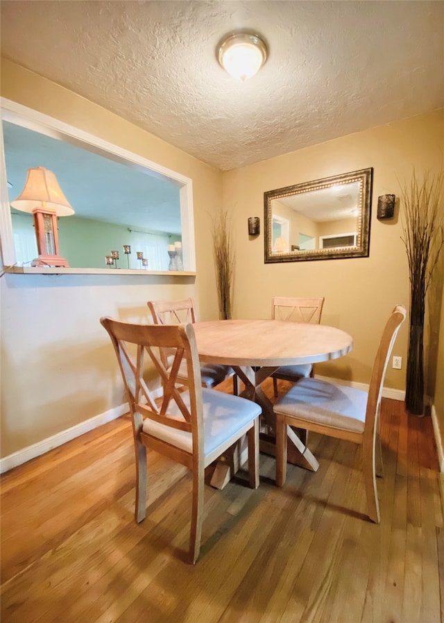 dining space featuring a textured ceiling, wood finished floors, and baseboards