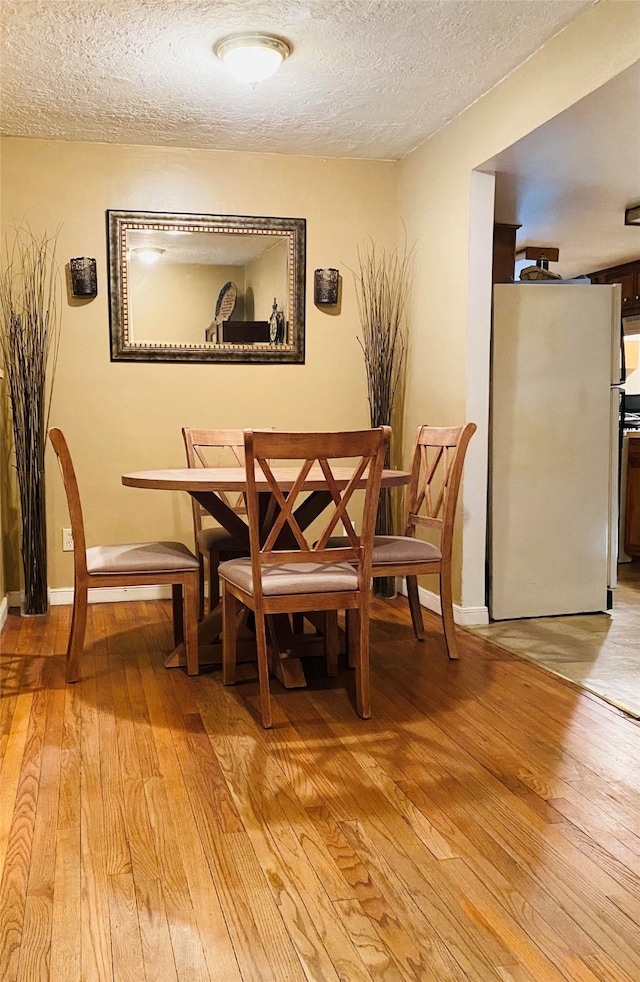 dining area featuring baseboards, light wood-style flooring, and a textured ceiling