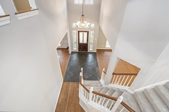 foyer with baseboards, a towering ceiling, wood finished floors, an inviting chandelier, and stairs