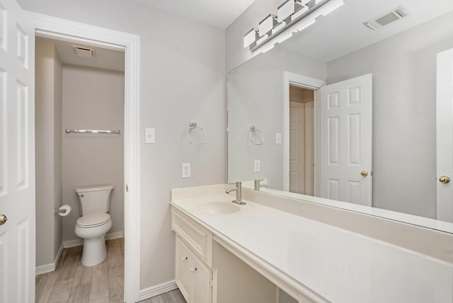 bathroom featuring baseboards, visible vents, toilet, wood finished floors, and vanity