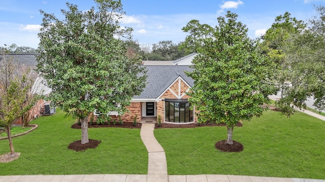 view of front of house with a shingled roof, a front lawn, cooling unit, and brick siding