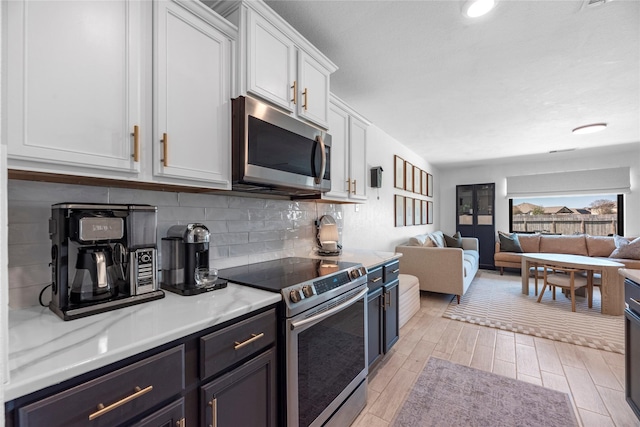 kitchen featuring stainless steel appliances, white cabinets, open floor plan, light wood finished floors, and tasteful backsplash