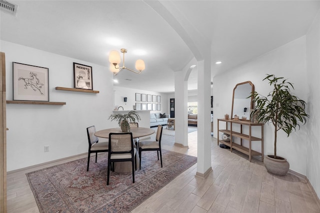 dining space featuring arched walkways, baseboards, visible vents, and light wood finished floors