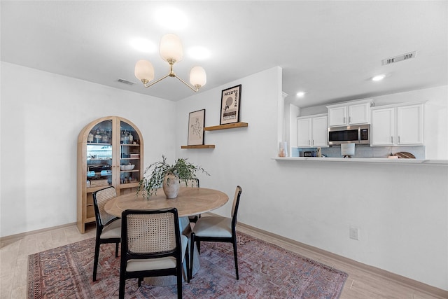 dining area with baseboards, light wood-type flooring, visible vents, and a notable chandelier