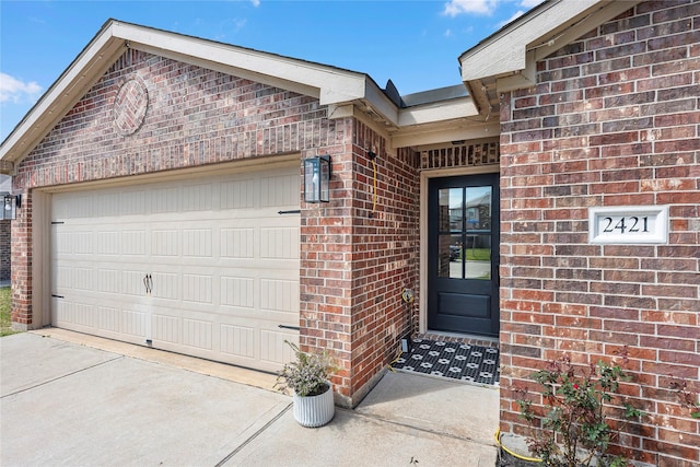 doorway to property featuring a garage, driveway, and brick siding