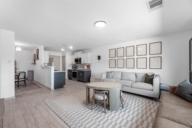 living area featuring light wood finished floors, visible vents, and baseboards