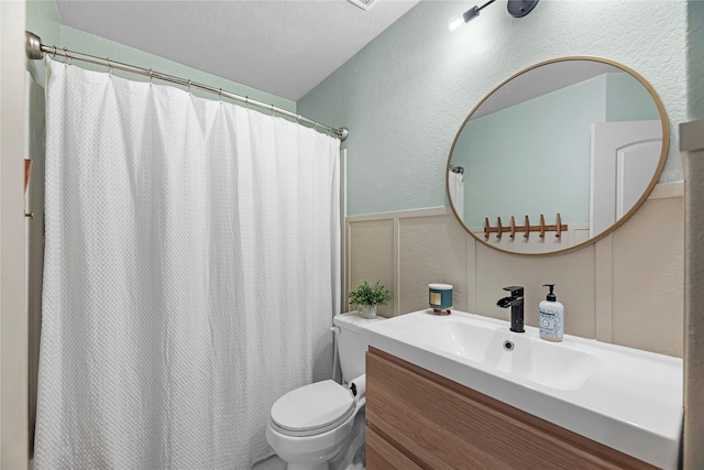 bathroom featuring a textured wall, toilet, a shower with curtain, vanity, and a decorative wall