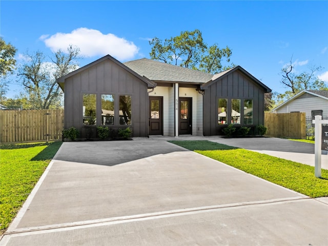 modern farmhouse with a shingled roof, board and batten siding, fence, driveway, and a front lawn