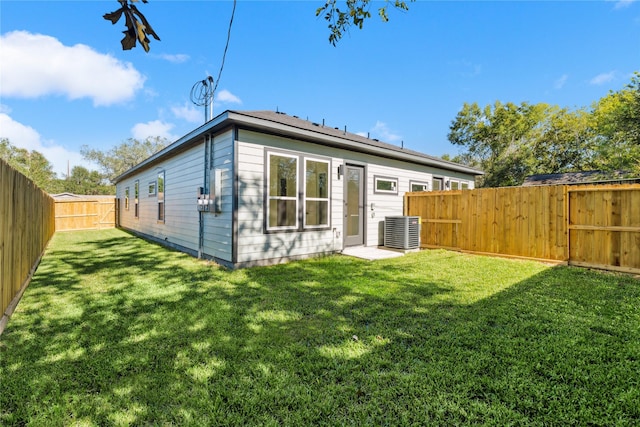 rear view of house with central air condition unit, a fenced backyard, and a yard