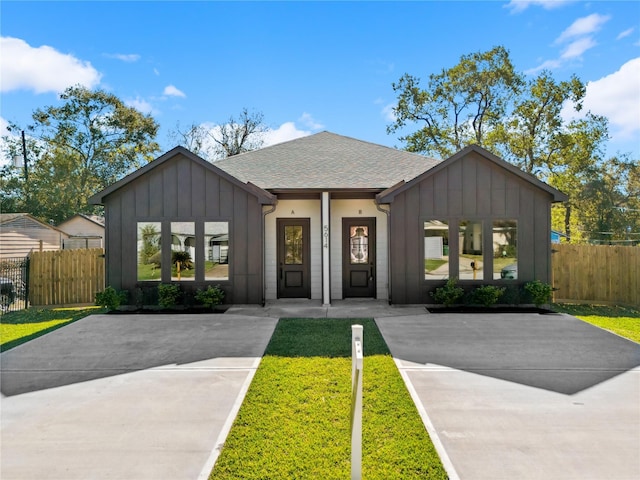 view of front of house featuring board and batten siding, roof with shingles, fence, and a front lawn