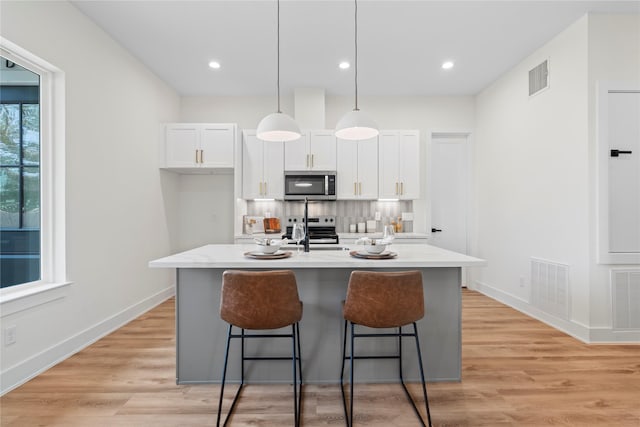 kitchen with stainless steel appliances, visible vents, light wood-style flooring, white cabinetry, and a kitchen breakfast bar