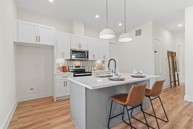 kitchen with stainless steel appliances, light wood finished floors, a sink, and visible vents