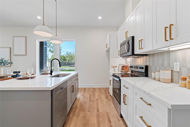 kitchen with a sink, light wood-style floors, appliances with stainless steel finishes, tasteful backsplash, and a center island with sink