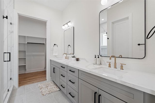 full bath featuring double vanity, a stall shower, a spacious closet, and a sink