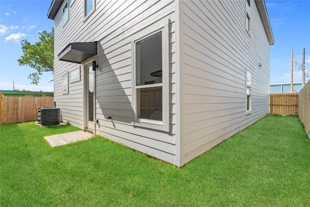 view of side of property with a fenced backyard, a yard, and central air condition unit