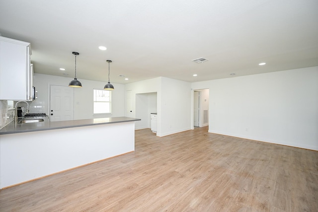 kitchen featuring visible vents, white cabinets, light wood-style flooring, pendant lighting, and a sink