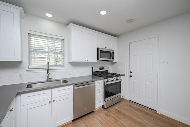 kitchen with stainless steel appliances, dark countertops, white cabinets, a sink, and light wood-type flooring