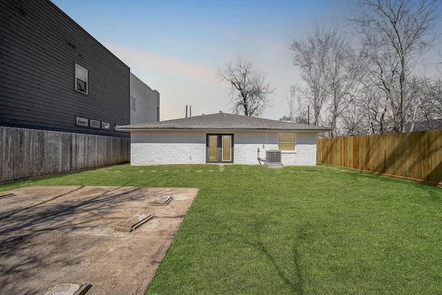 rear view of property with a yard, brick siding, cooling unit, and fence