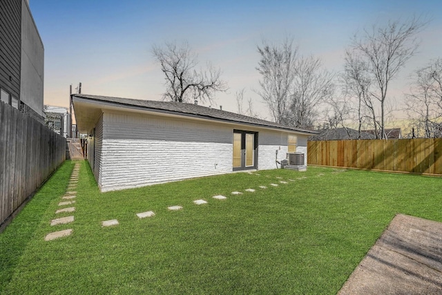 rear view of property with central air condition unit, a fenced backyard, a lawn, and brick siding