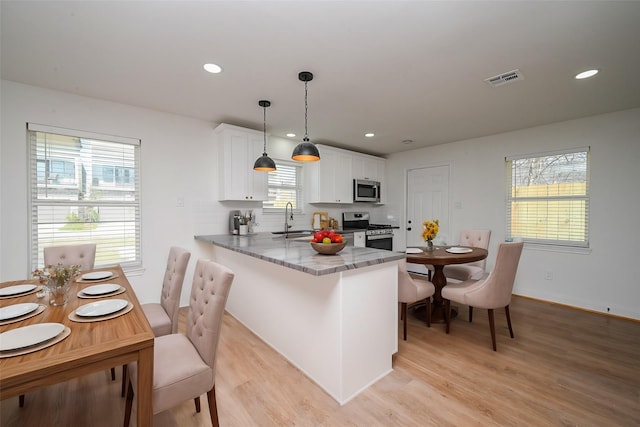 kitchen featuring stainless steel appliances, light wood-style flooring, white cabinets, a sink, and a peninsula