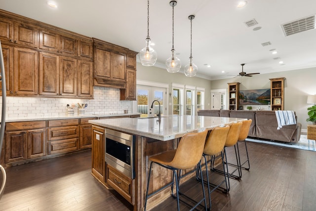kitchen featuring a breakfast bar area, visible vents, backsplash, stainless steel microwave, and dark wood finished floors