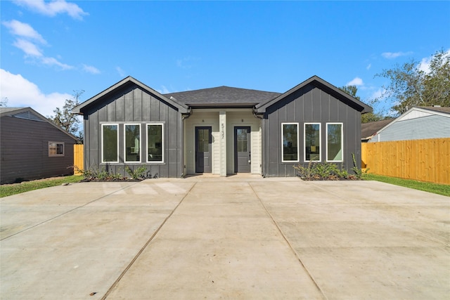 view of front of home with roof with shingles, board and batten siding, a patio area, and fence