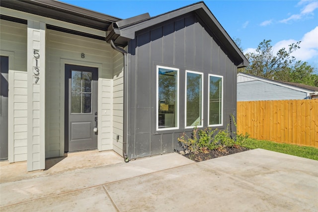 property entrance featuring a patio, board and batten siding, and fence