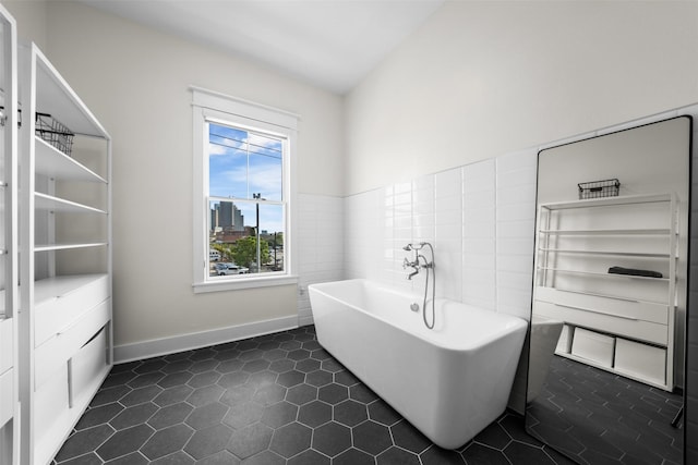 bathroom featuring a freestanding tub, tile patterned flooring, baseboards, and tile walls