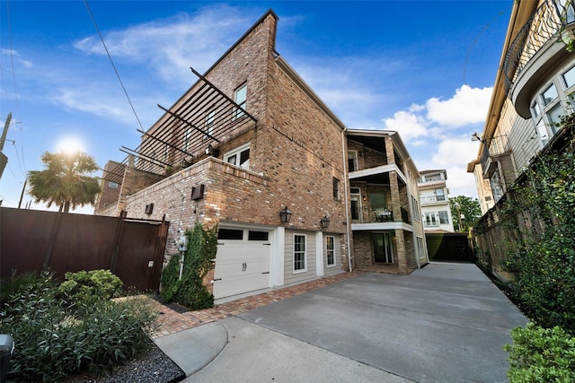 view of home's exterior featuring a balcony, a garage, brick siding, fence, and driveway