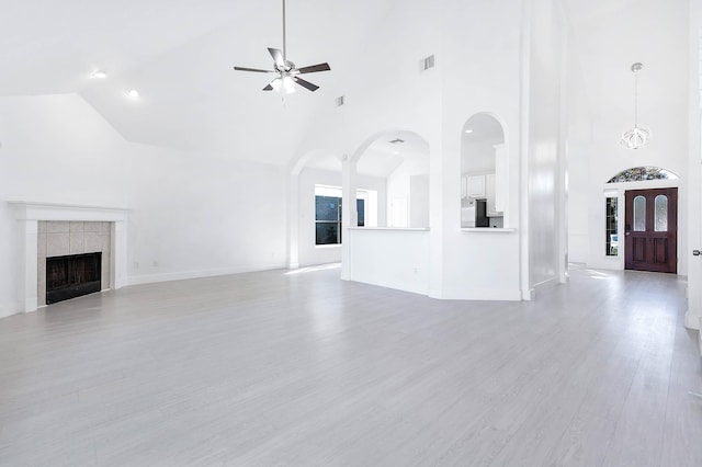 unfurnished living room with light wood finished floors, visible vents, a tile fireplace, high vaulted ceiling, and ceiling fan with notable chandelier