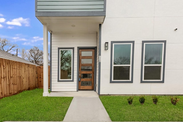 entrance to property featuring a yard, fence, and stucco siding